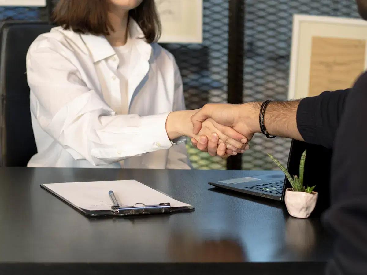 Counsellor and student shaking hands across a desk over application paperwork